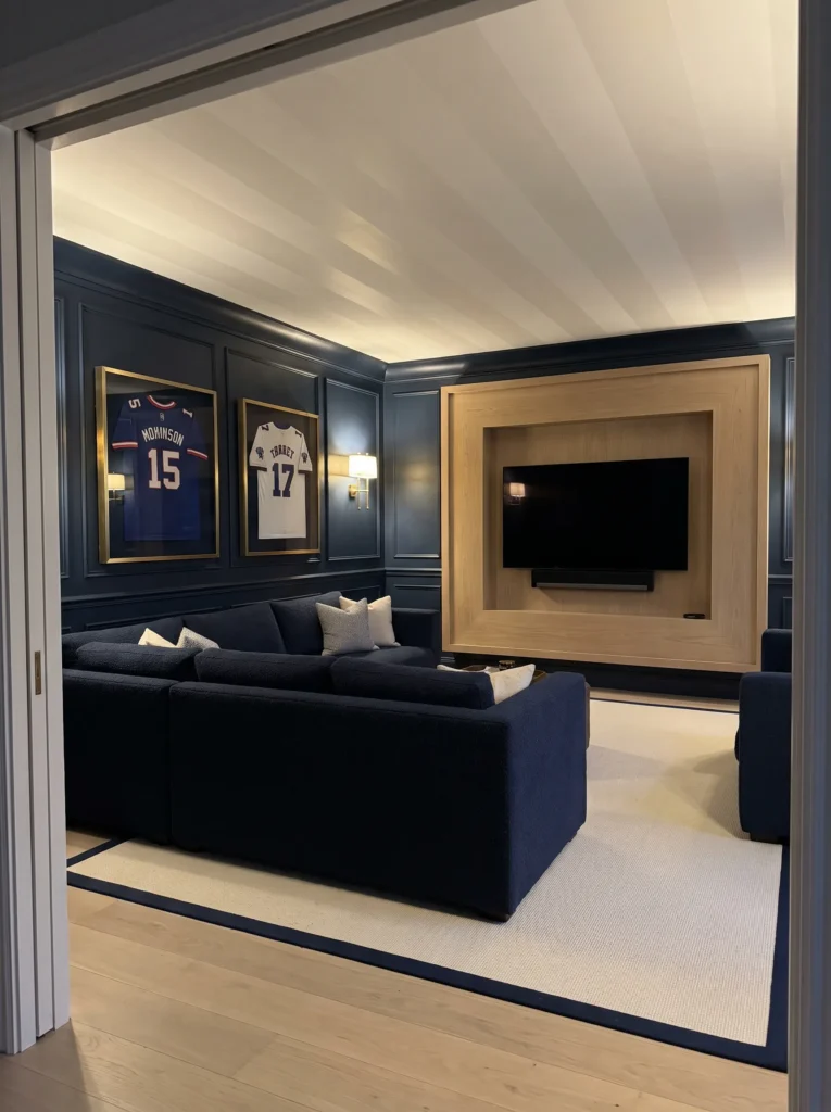"Navy sports lounge with framed jerseys and white oak media wall"