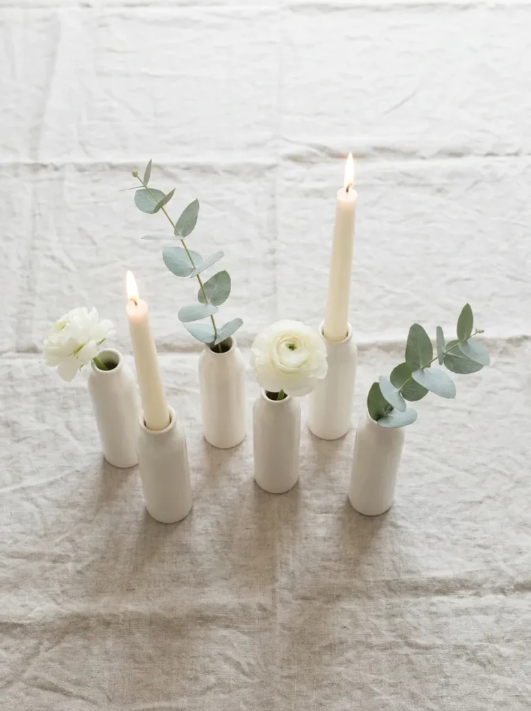 Five slim ivory bud vases in an irregular line, each with a single eucalyptus or ranunculus stem