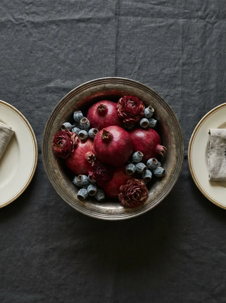 Tarnished silver bowl filled with pomegranates and dried burgundy ranunculus