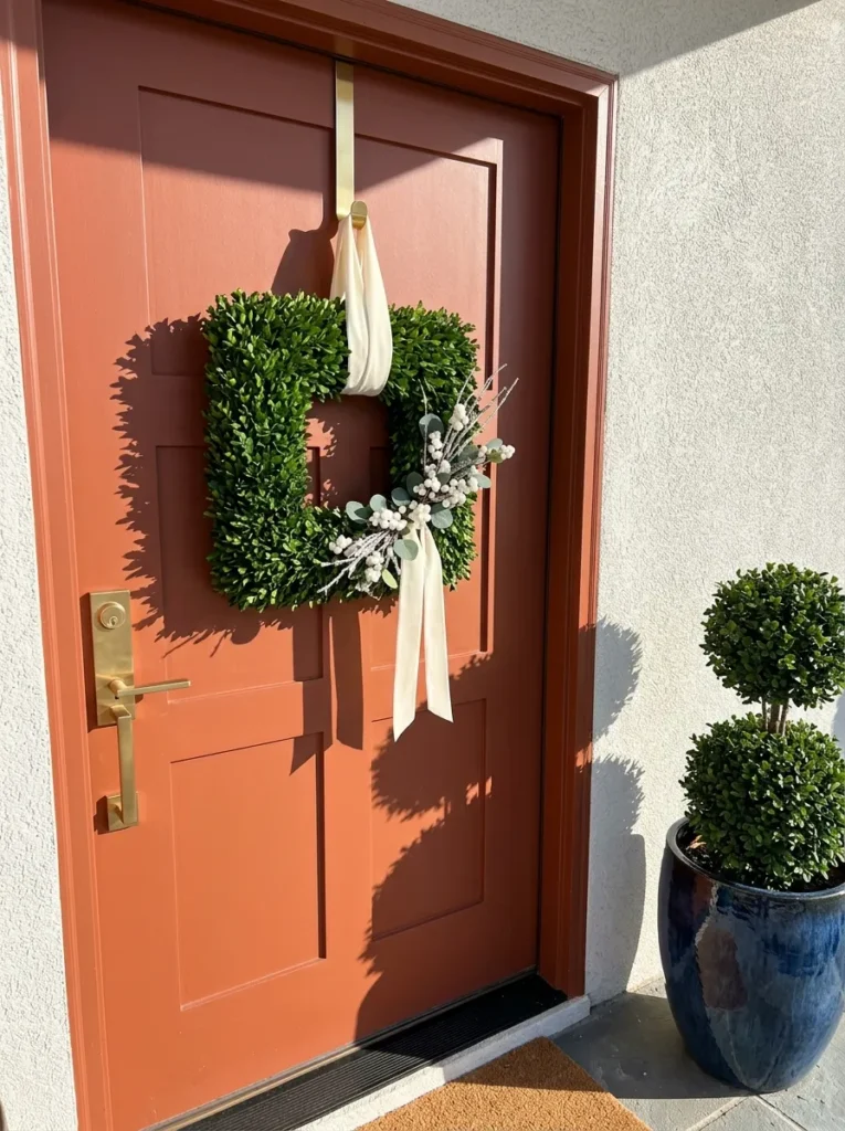 "Square faux boxwood wreath with ivory velvet loop on a terracotta door"